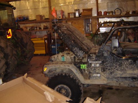 1992 Ford Bronco - Muddy Jeep Wrangler in a garage with the hood up, next to a tractor. Visible badges include 'Wrangler X' and 'Jeep'.