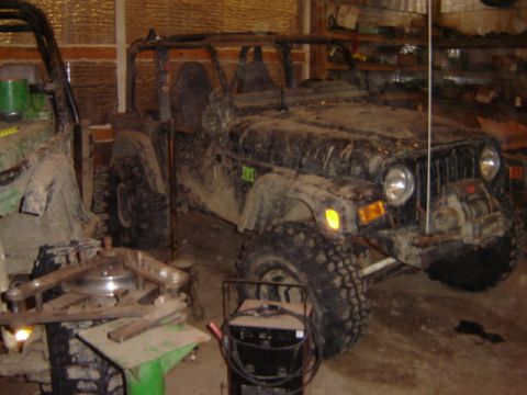 1992 Ford Bronco - Two off-road vehicles are parked inside a garage, covered in mud.