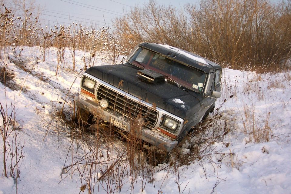 Dark 1970s Ford Bronco nosed into a snowy ditch among dead brush