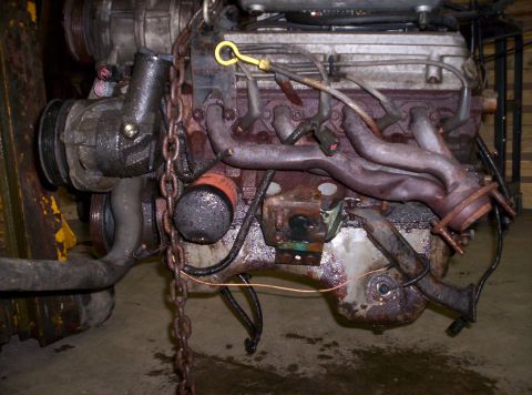 1993 Ford Bronco - Close-up of a V8 engine, showing exhaust pipes, oil filter, and a hanging chain.