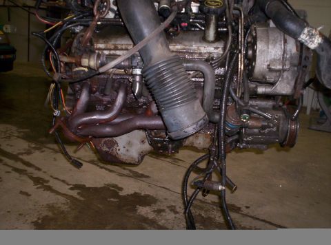 1993 Ford Bronco - Engine assembly with visible exhaust manifold and air intake hose, showing signs of wear and tear.