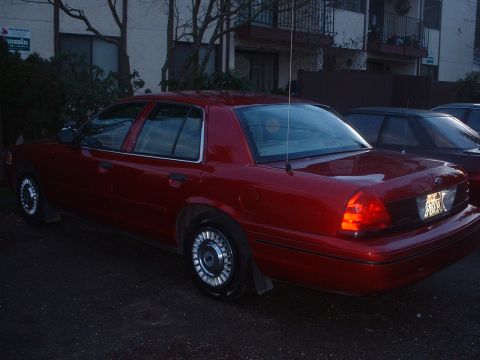 1999 Ford Crown Victoria - Rear view of a red sedan, parked next to another vehicle.