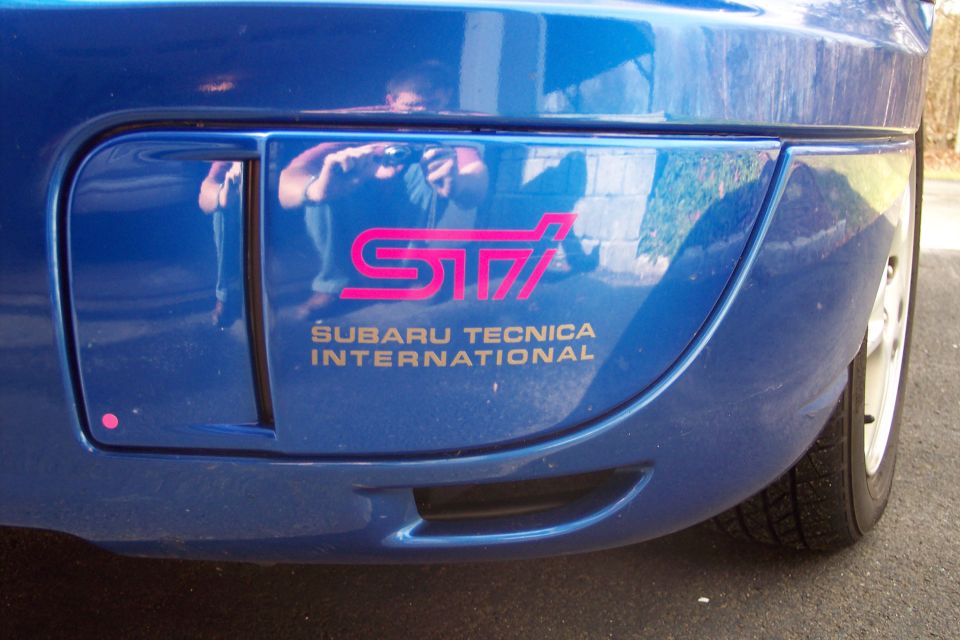 Pink STI and gold Subaru Tecnica International decal on blue rear bumper corner