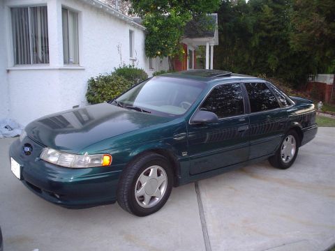 1993 Ford Taurus - This green sedan, likely a 1996 model, is parked in a driveway with tinted windows.