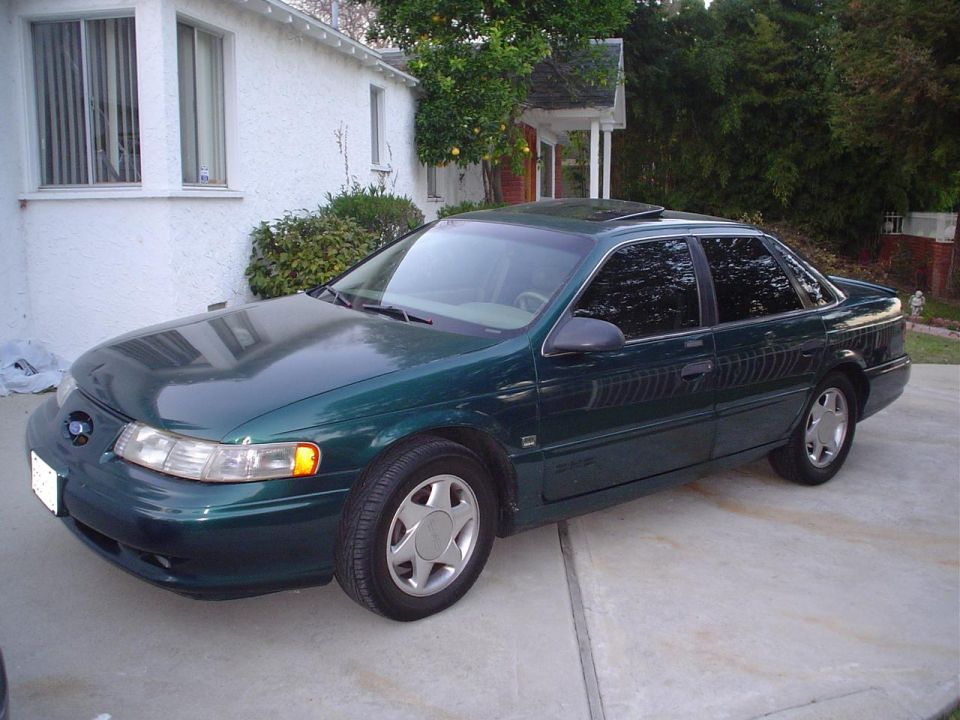 Dark green Ford Taurus SHO sedan in driveway, front 3/4 driver-side view with sunroof and alloys