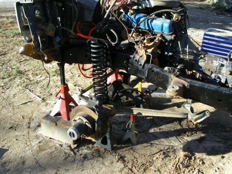 1985 Ford Bronco - The vehicle's front end is disassembled and supported by jack stands, revealing the engine and suspension components.