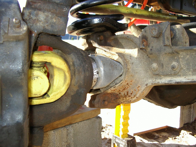 Close-up of a yellow driveshaft U-joint connected to a differential housing with a black coil spring above