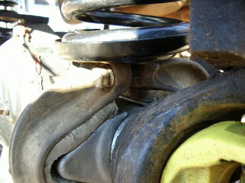 1985 Ford Bronco - This image shows a close-up view of a vehicle's suspension system, focusing on the coil spring and surrounding metal parts.