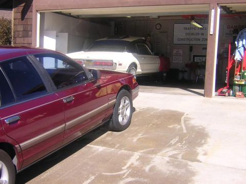 1992 Ford Crown Victoria - A dark maroon Ford Crown Victoria sedan viewed from the rear driver's side, parked on a concrete driveway in front of an open garage. Insid…