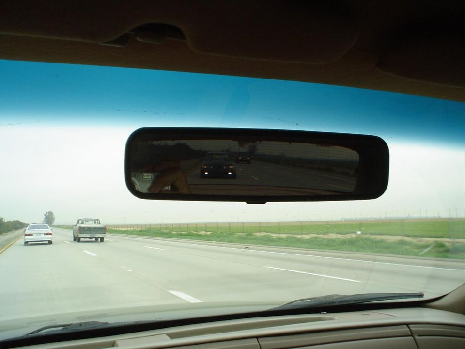 Reflection of a 1993 Ford Taurus in the rearview mirror, driving on a highway