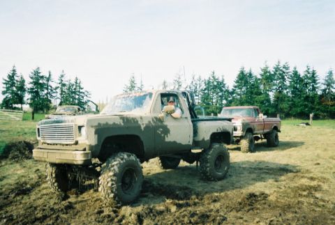 1976 Chevrolet C/K Pickup - Two lifted pickup trucks are covered in mud, suggesting an off-road adventure.