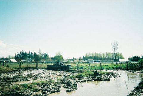1976 Chevrolet C/K Pickup - A pickup truck is stuck in a muddy field, with a rural landscape behind it.