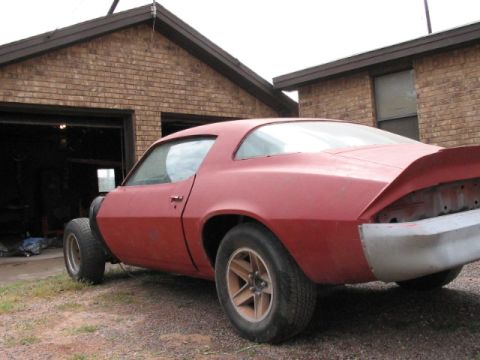 1979 Chevrolet Camaro - This red coupe, likely from the early 1970s, is parked in front of a brick garage and appears to be in the process of restoration.