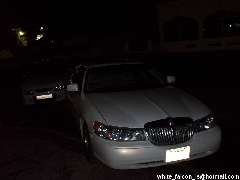 White Lincoln Town Car front view at night, with another car behind