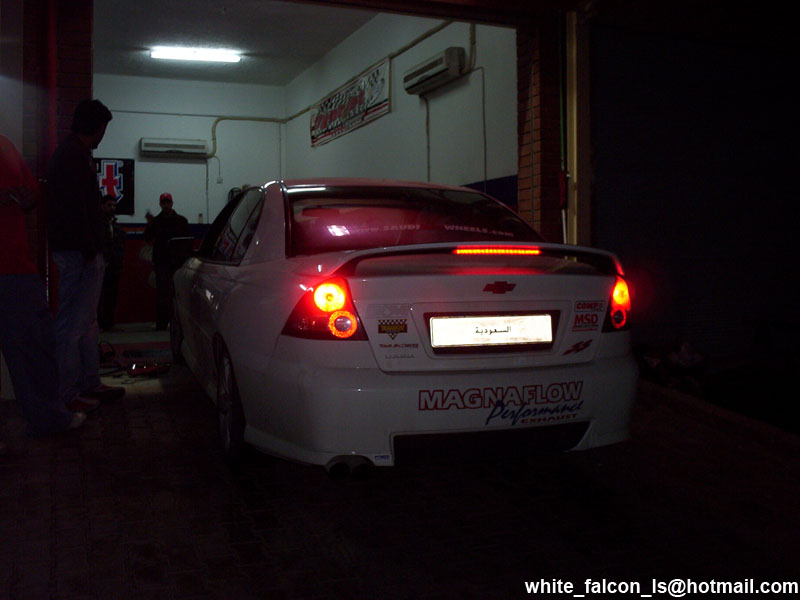 White sedan with a spoiler and aftermarket exhaust, rear view. Magnaflow sticker on trunk