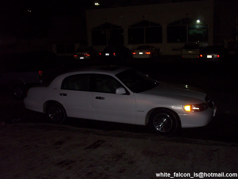 White sedan parked at night. Other cars and a building are in the background