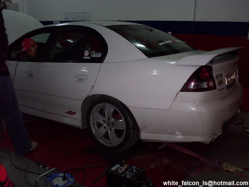 White sedan with a spoiler on a dynamometer, rear view