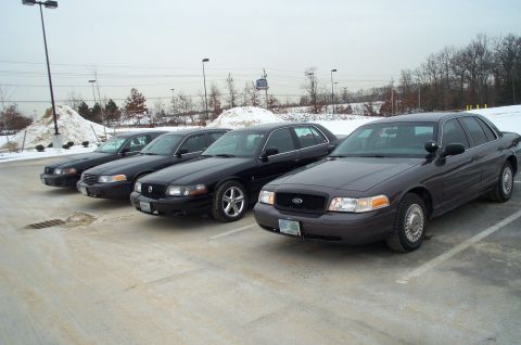 2001 Ford Crown Victoria - A line of four Ford Crown Victoria police sedans are parked in a lot during winter.