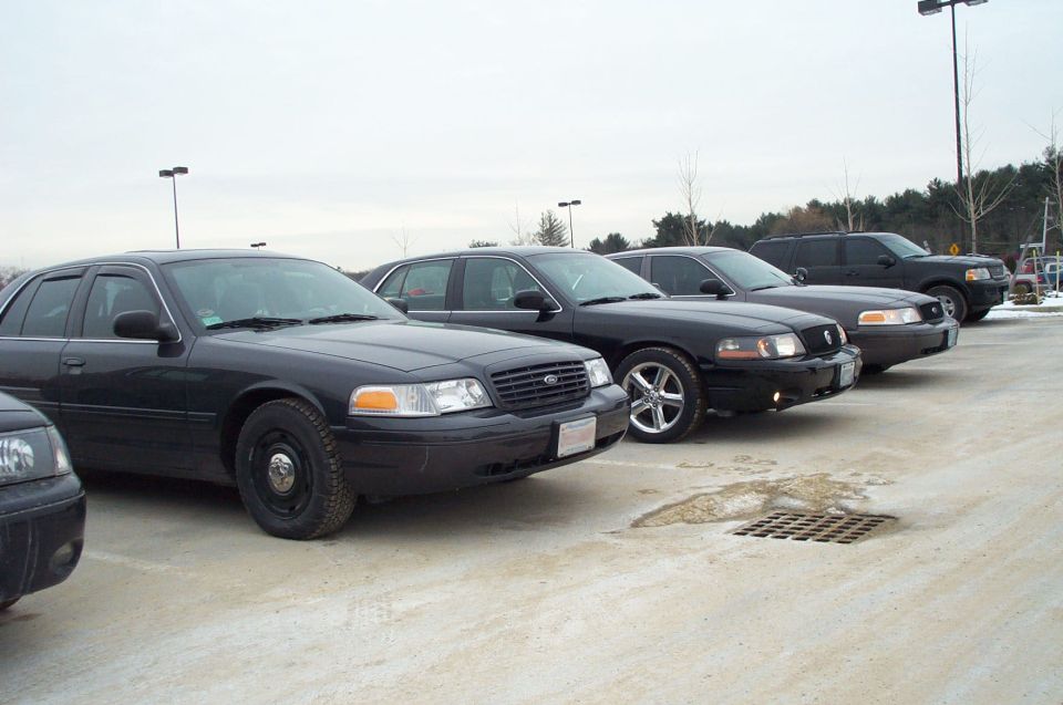 Row of black Ford Crown Victorias parked in a lot, one in foreground
