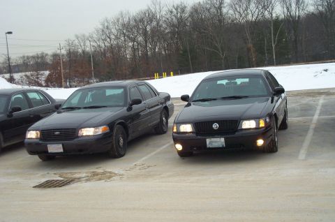 2001 Ford Crown Victoria - Two black sedans, one appearing to be a Ford Crown Victoria and the other a Mercury Grand Marquis, are parked side-by-side in a snowy lot.