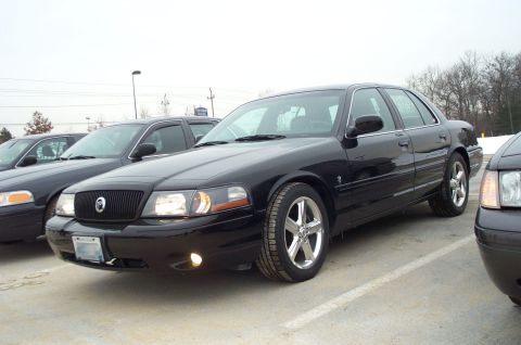 2001 Ford Crown Victoria - Three black sedans, including a 2001 Ford Crown Victoria, are parked in an outdoor lot.