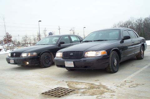 2001 Ford Crown Victoria - Two black 2001 Ford Crown Victoria police cars are parked in a lot on an overcast day.