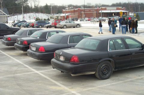 2001 Ford Crown Victoria - Several black Ford Crown Victorias are parked in a lot on a cloudy day.
