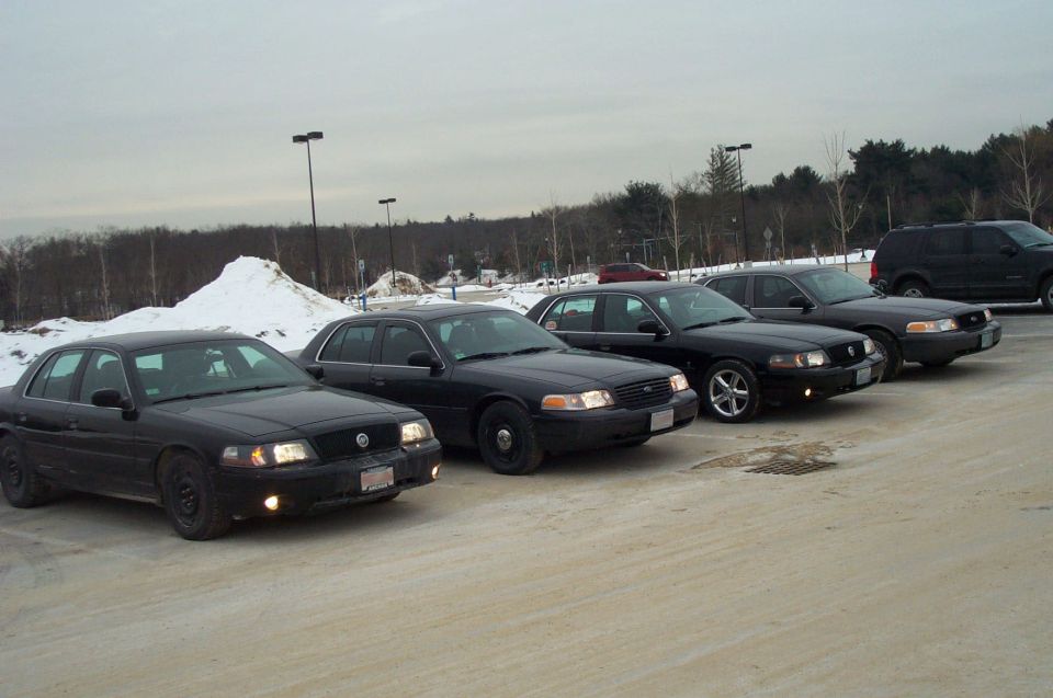 Four black 2001 Ford Crown Victorias parked in a lot