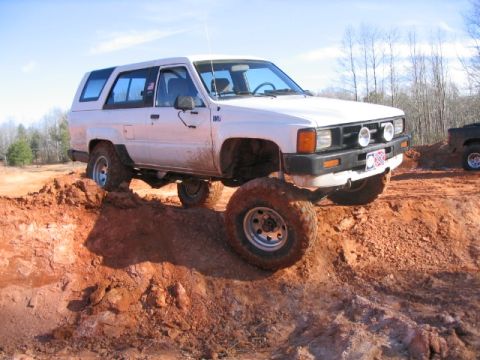1986 Ford F-150 - White Toyota 4Runner tackles an off-road obstacle, with another vehicle in the background.
