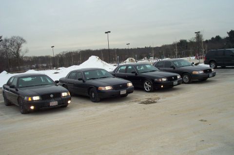 2001 Ford Crown Victoria - Four black Ford Crown Victoria sedans are parked in a lot during winter.