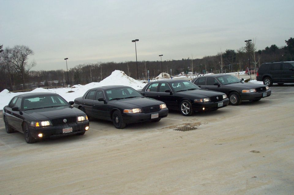 Four black Ford Crown Victoria sedans parked in a snowy lot