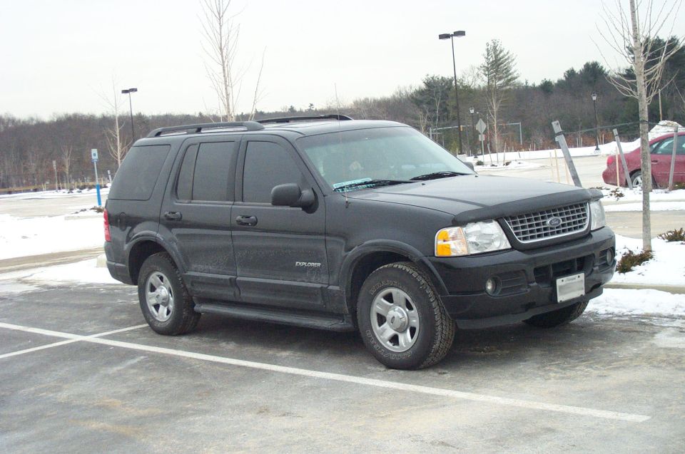 Black Ford Explorer parked in a lot with snow on the ground. It has a roof rack and a bug deflector on the hood