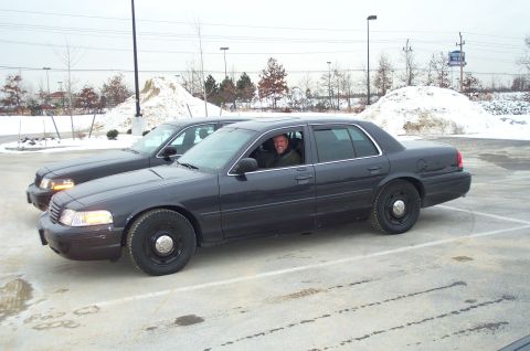 2001 Ford Crown Victoria - Two dark gray Ford Crown Victorias are parked side-by-side in a snowy parking lot.