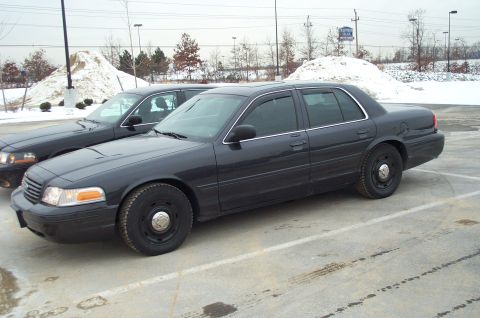 2001 Ford Crown Victoria - A dark 2001 Ford Crown Victoria sedan is parked in a lot during winter, with another similar vehicle visible behind it.