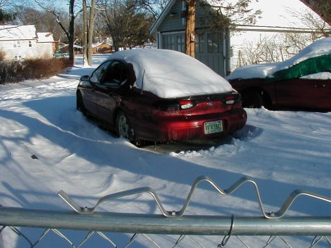 1997 Ford Taurus - A red 1997 Ford Taurus sits partially covered in snow on a winter day. Another vehicle is visible to the right, also covered in snow.