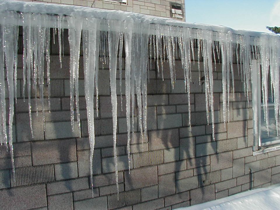Icicles hanging from a roof over a brick wall