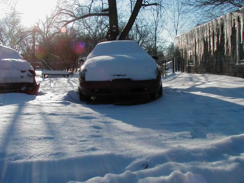 1997 Ford Taurus - Two vehicles are parked in a snowy yard with icicles hanging from the roof of a nearby building.