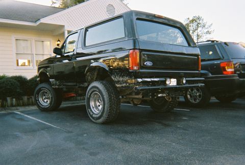 1996 Ford Bronco - This black Ford Bronco is parked in a lot next to another vehicle, showing its rear end.