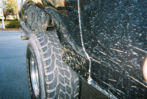1996 Ford Bronco - A black SUV's side panel and tire are heavily splattered with mud, indicating off-road use.