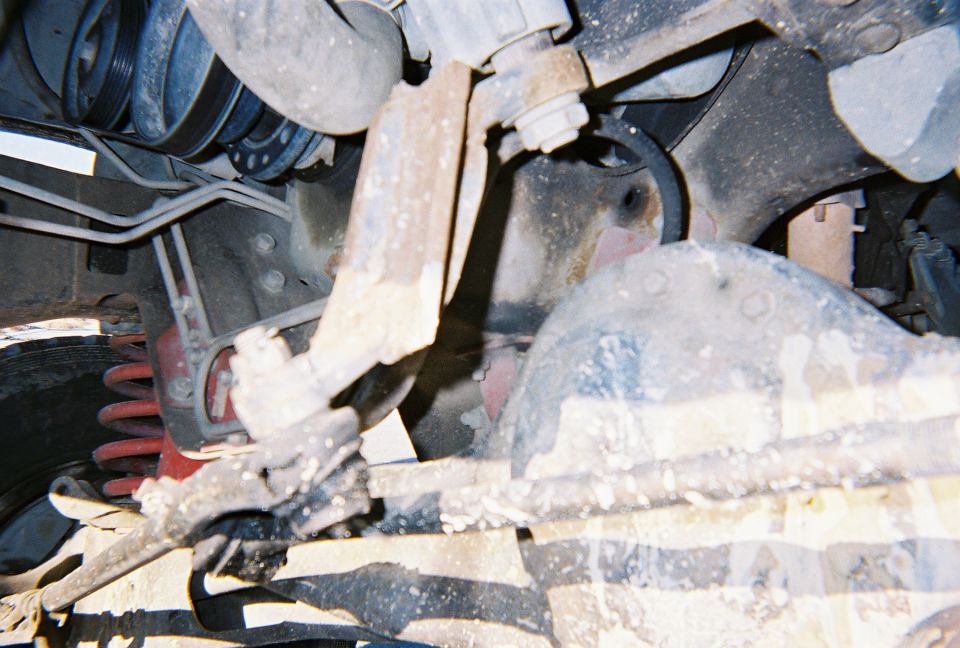 Close-up of rusty suspension parts, hoses, and engine components under a vehicle