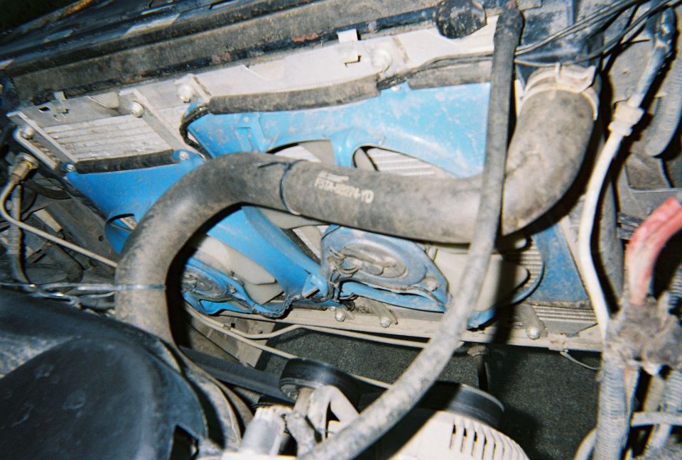 Engine bay view showing radiator, hoses, and fan. A blue bracket is visible behind the fan