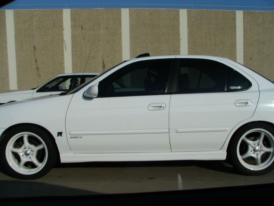 White Nissan Sentra Spec V sedan side view with white wheels on a highway next to a concrete wall