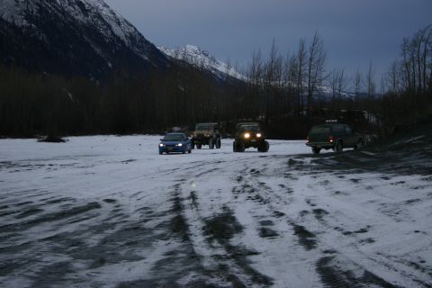 2003 Jeep TJ - Several vehicles traverse a snowy path near a wooded area with mountains looming in the distance.