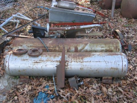 1989 Ford F-150 - Various pieces of scrap metal, including large cylindrical tanks, are scattered on the ground covered with leaves.