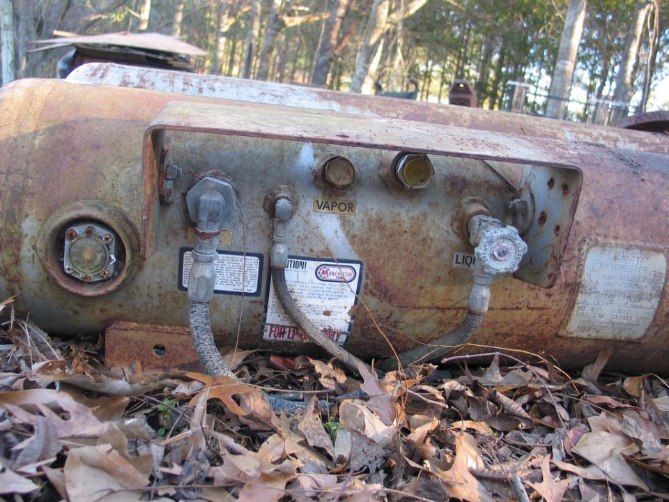 rusty propane tank with vapor and liquid valves, and a warning label