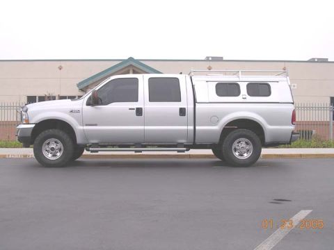 2004 Ford F-250 - A silver 2004 Ford F-250 Super Duty pickup truck is shown from the side, equipped with a camper shell and roof rack.