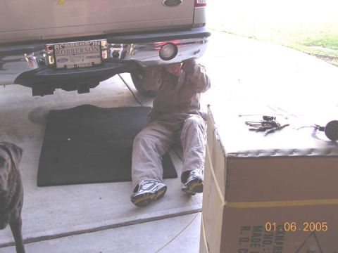 2004 Ford F-250 - Mechanic works on the rear bumper and hitch assembly of a 2004 Ford F-250 pickup truck.