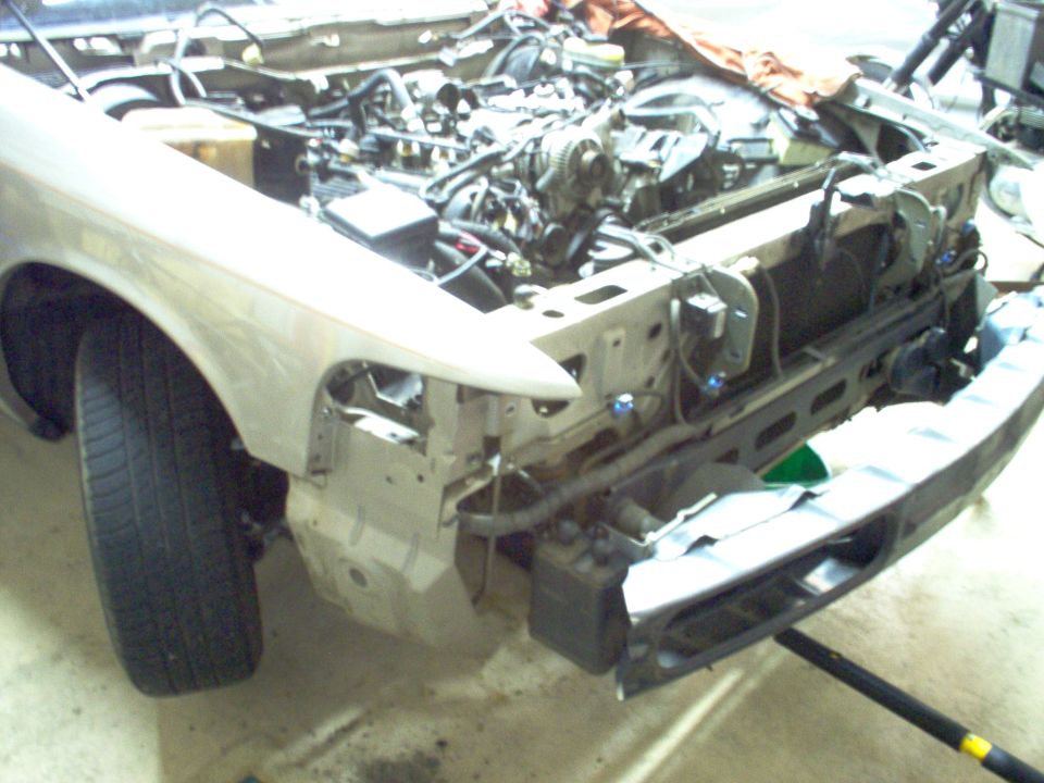 Silver sedan with front end stripped, exposed engine bay and radiator support in a garage