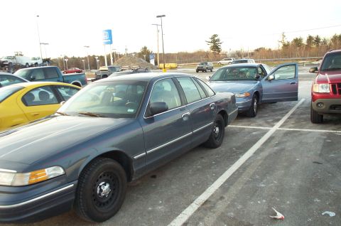 2001 Ford Crown Victoria - A dark blue sedan, identified as a 2001 Ford Crown Victoria, is parked in a lot with other vehicles.