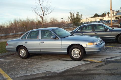 2001 Ford Crown Victoria - Two sedans, a light blue 2001 Ford Crown Victoria and a dark gray one, are parked side-by-side.
